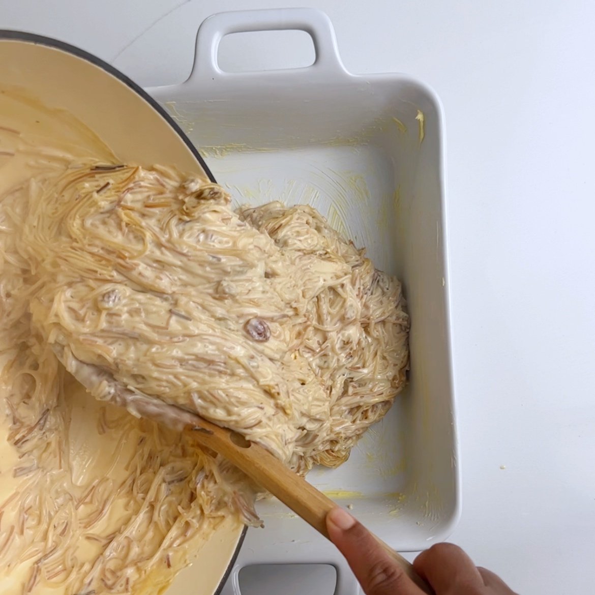 pouring vermicelli noodles from a cream dutch oven into a greased rectangular casserole dish