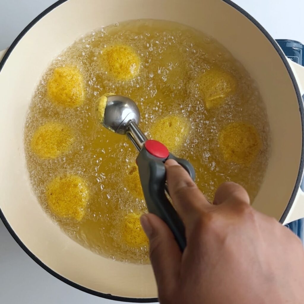 Dropping batter into hot oil using a silver and gray cooking scoop with a red button