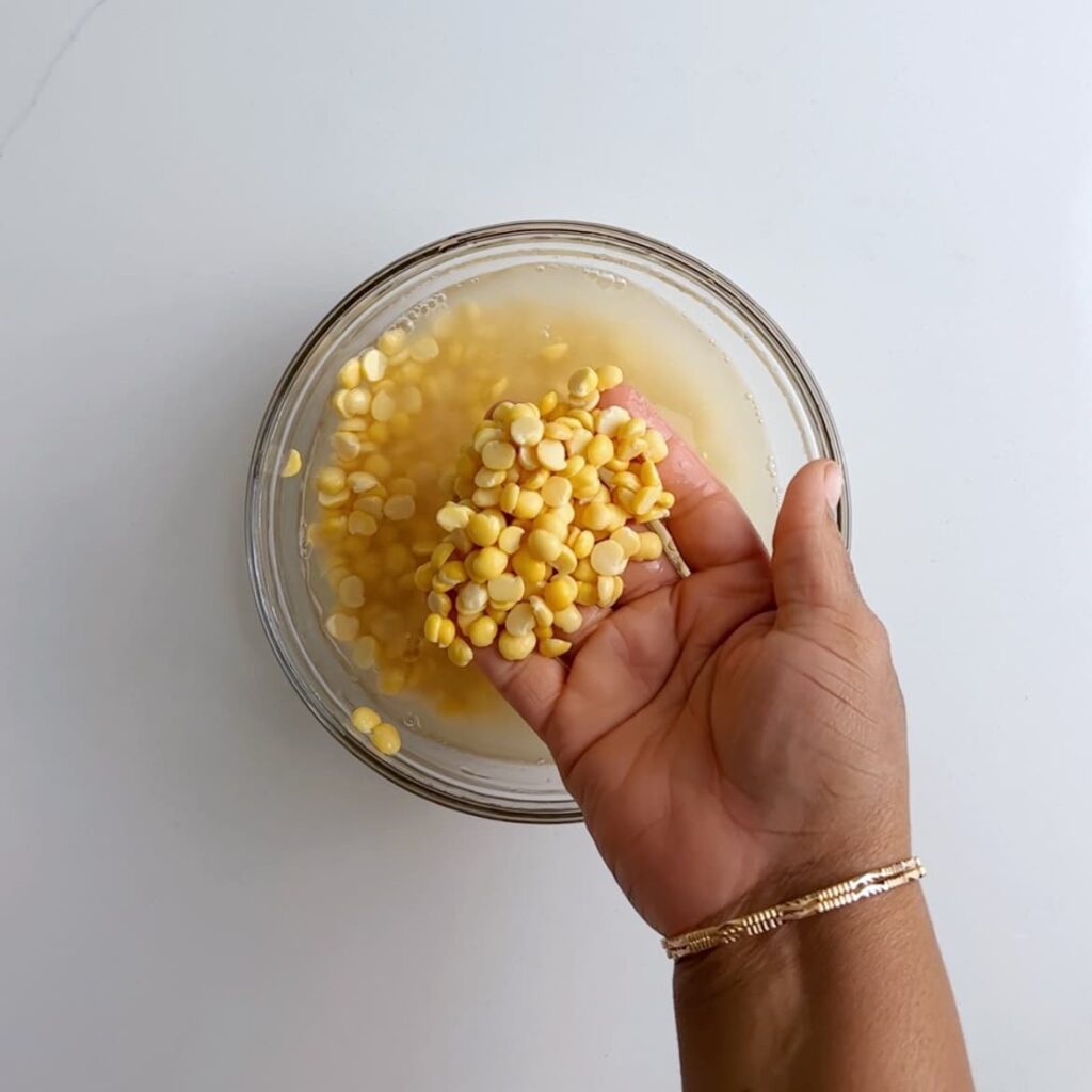 split peas in a bowl of water being scooped by a brown hand