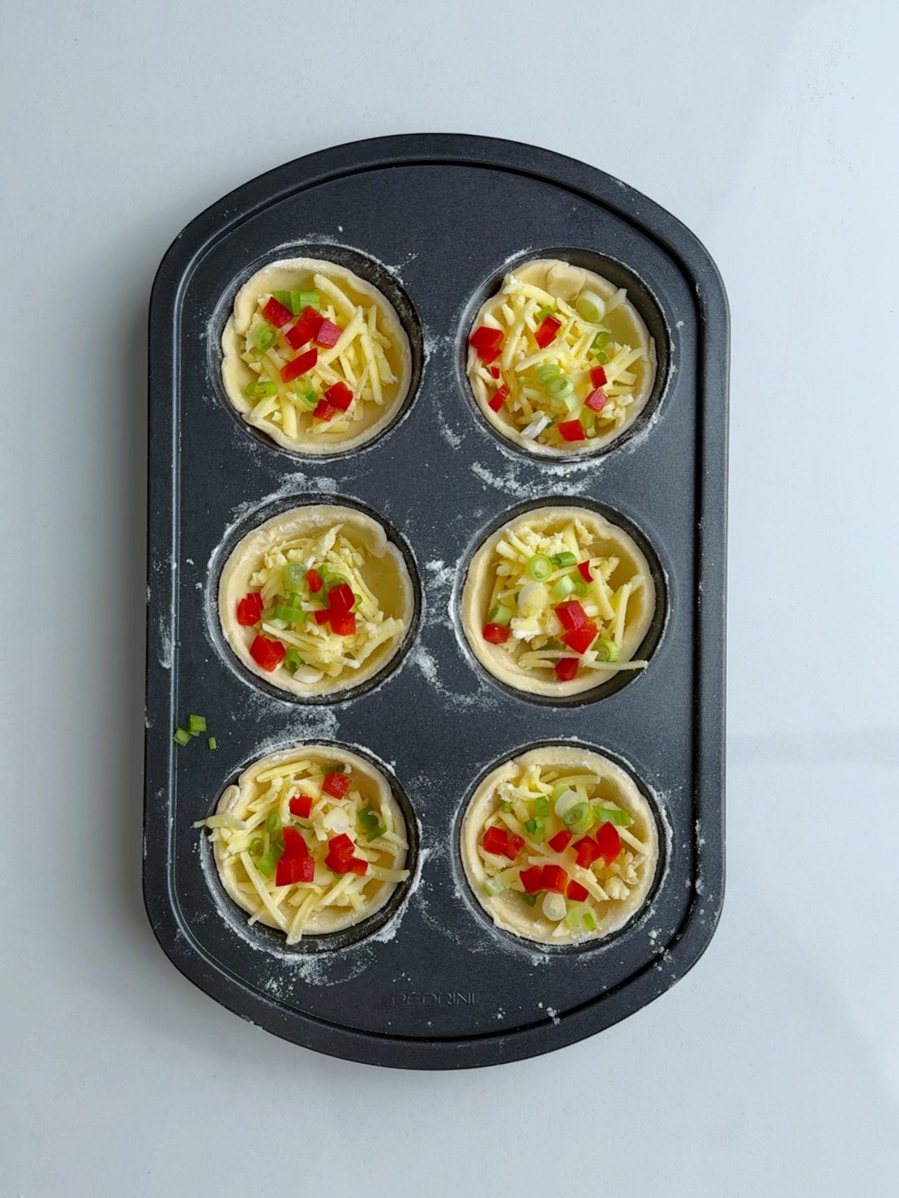 Red bell peppers finely diced, scallions and shredded cheese added to a muffin tin