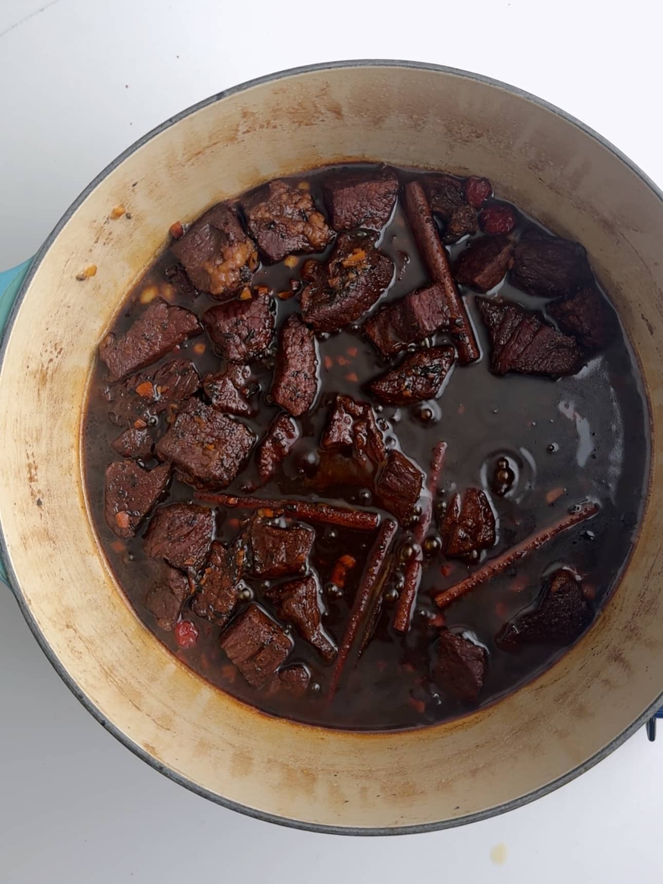 Beef in a large stock pot with cinnamon and spices and cassareep that is making it dark.