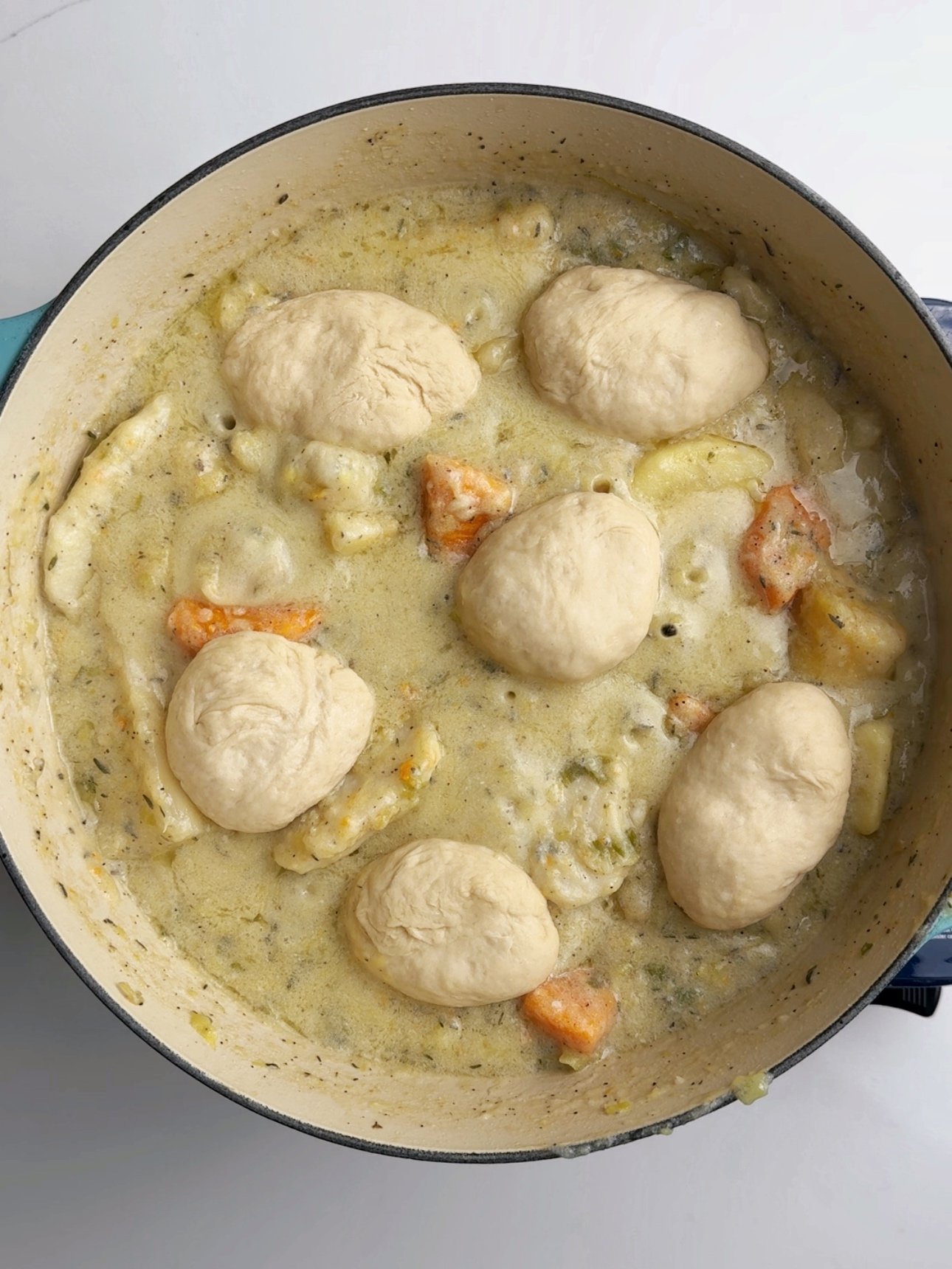 Cooked metemgee in a Dutch oven with soft dumplings, sliced root vegetables, and chunks of sweet potato in a thick coconut broth.