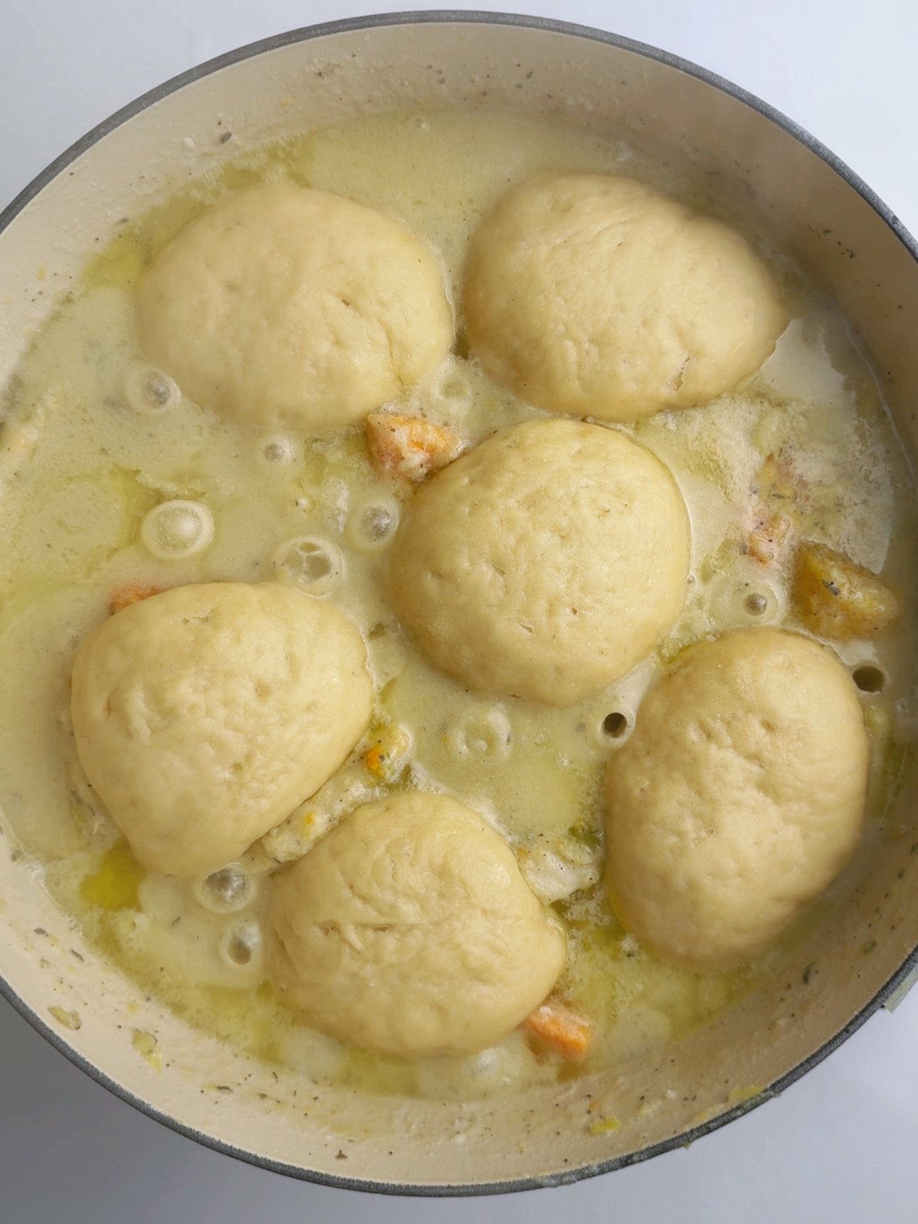 Dumplings simmering in a creamy coconut broth with chunks of root vegetables in a large Dutch oven.