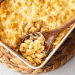 Close-up of a wooden spoon lifting creamy 5 cheese mac and cheese from a baking dish