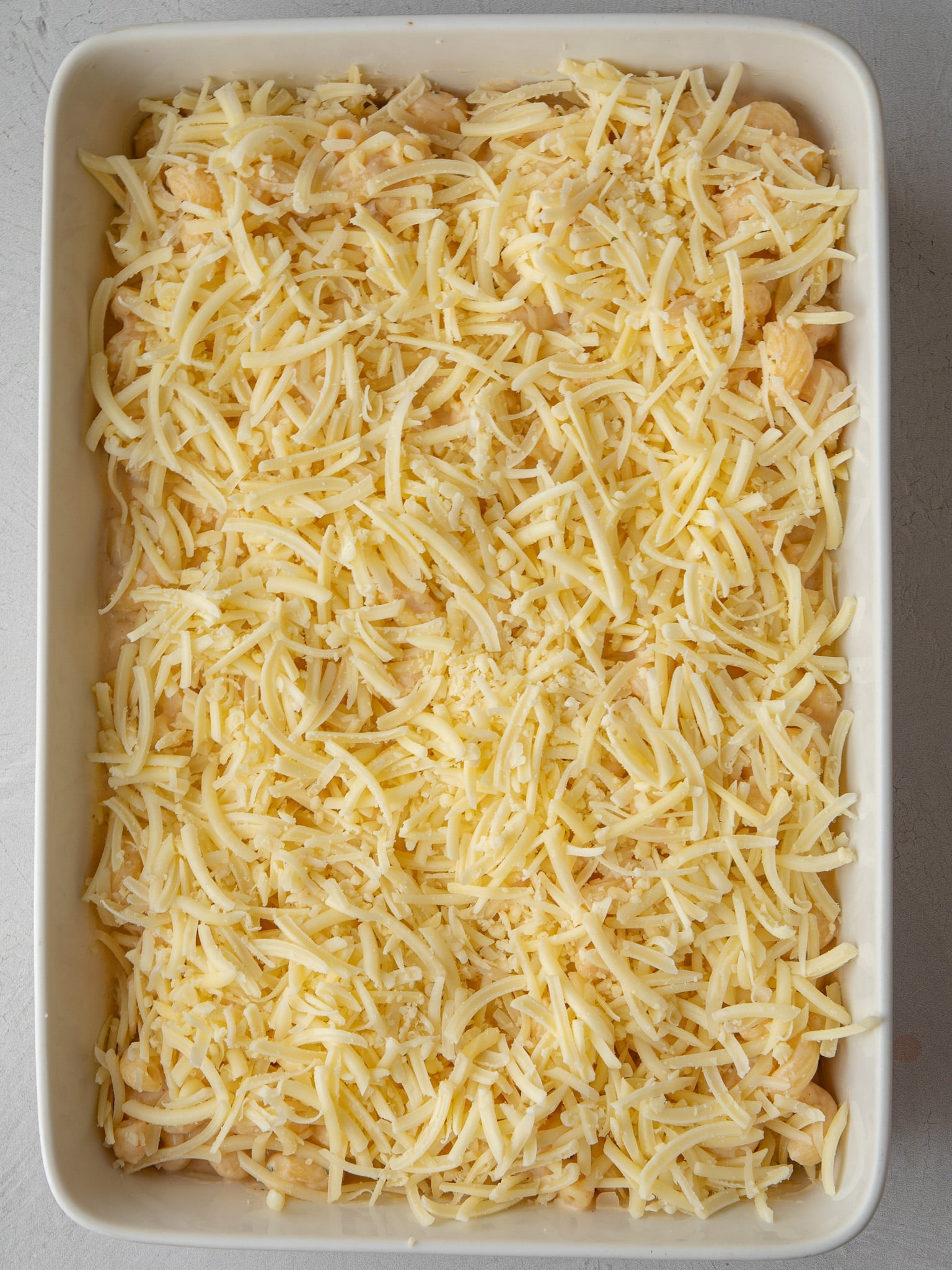 Unbaked mac and cheese topped with shredded cheddar