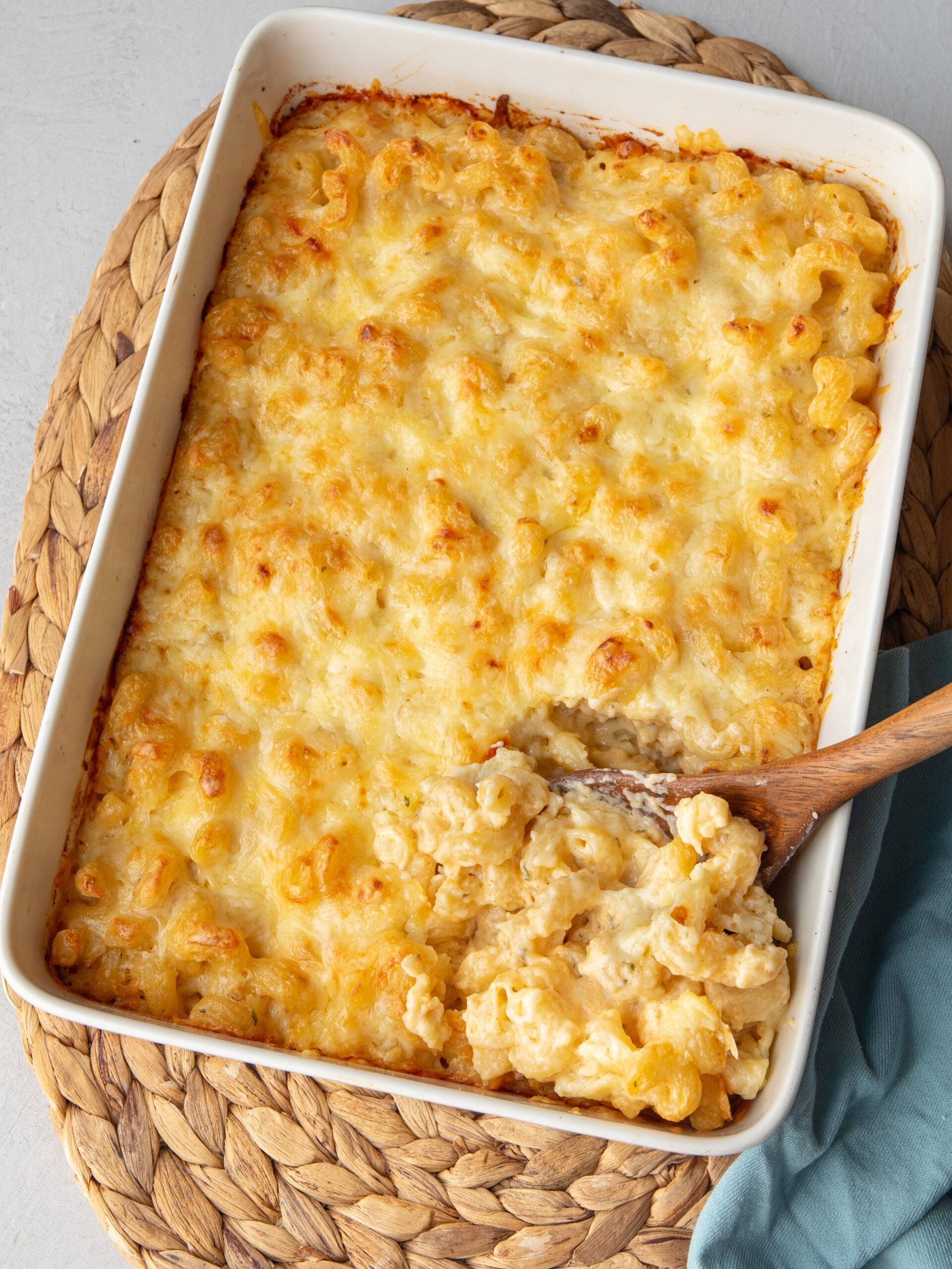 Baked 5 cheese mac and cheese in a white 9×13 dish with a golden cheese top and a wooden spoon scooping out a creamy serving.