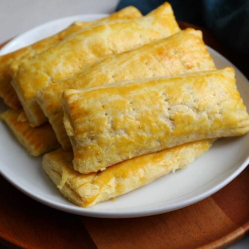 Guyanese cheese rolls stacked up on a white plate resting on a wooden plate.