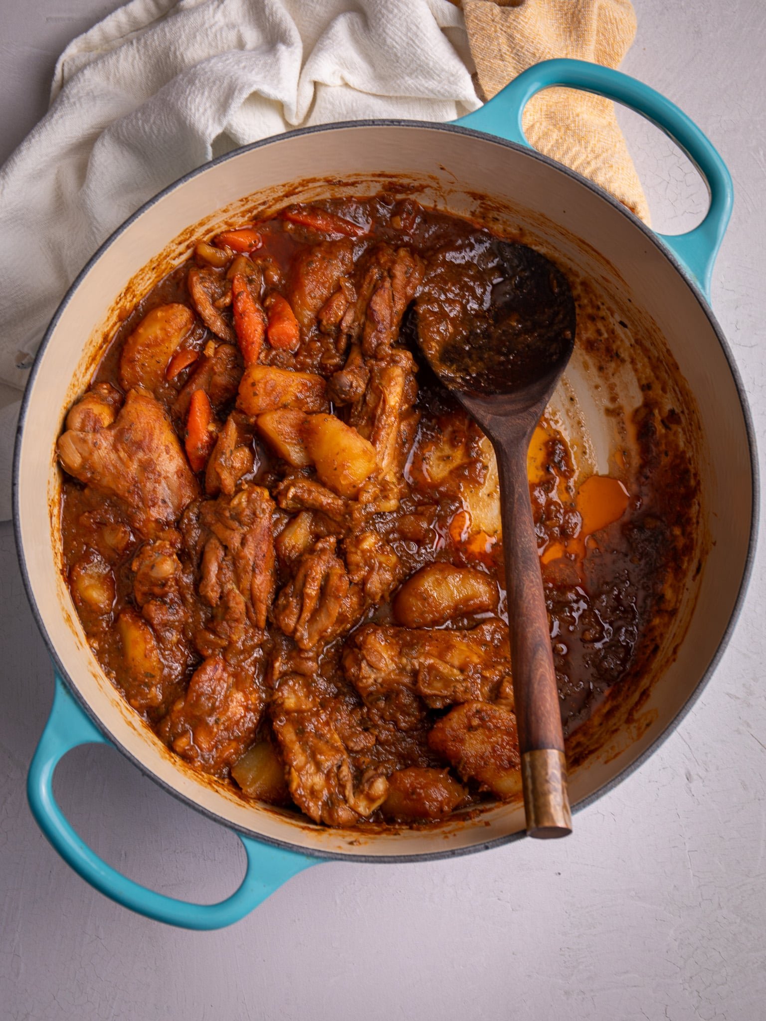 Guyanese Chicken stew in a large dutch pot with blue handles. A wooden spoon is resting in the pot in a place where stew would have been scooped from the pot. 