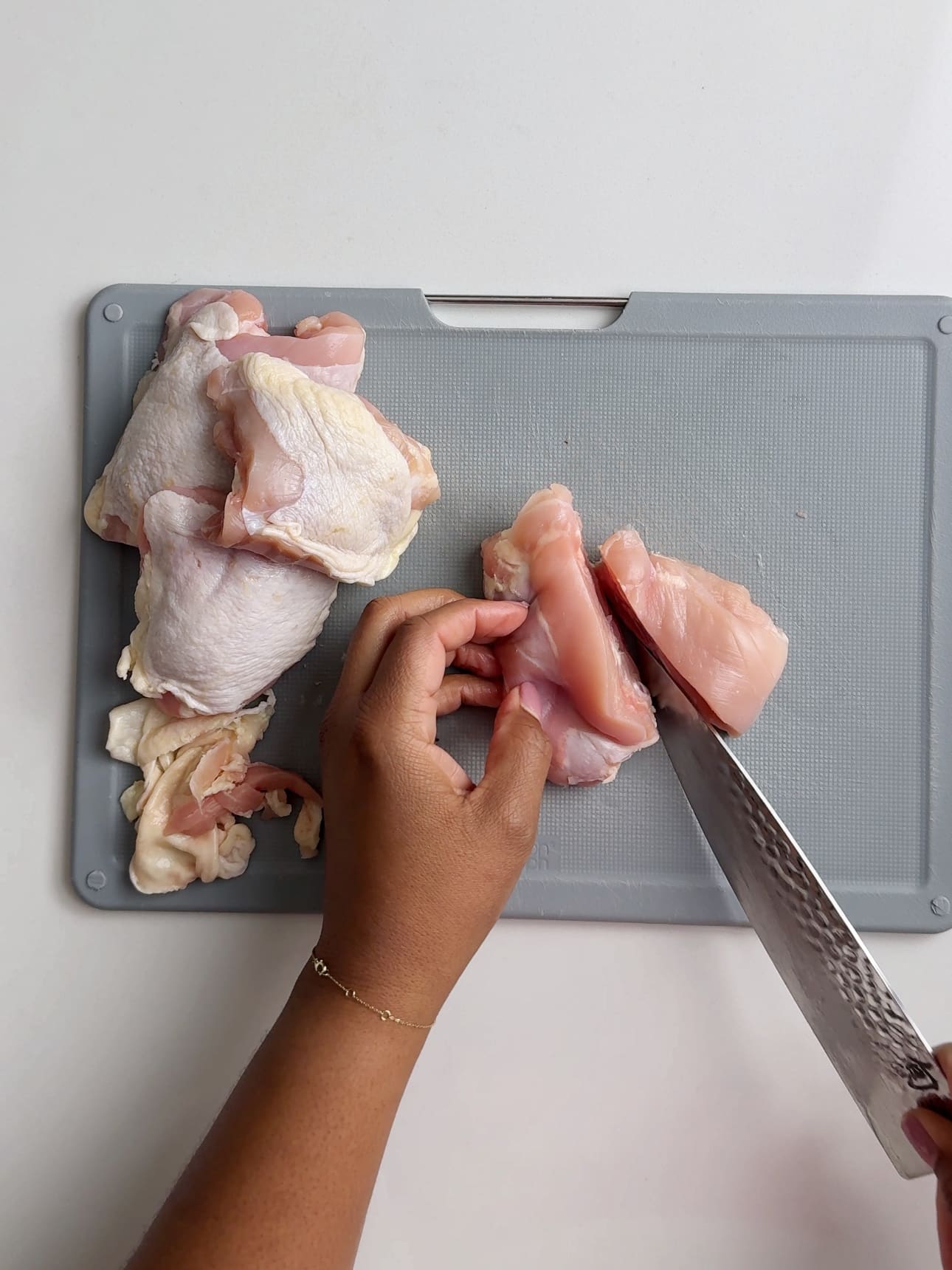 Cutting a chicken thigh in half on a grey plastic cutting board. 