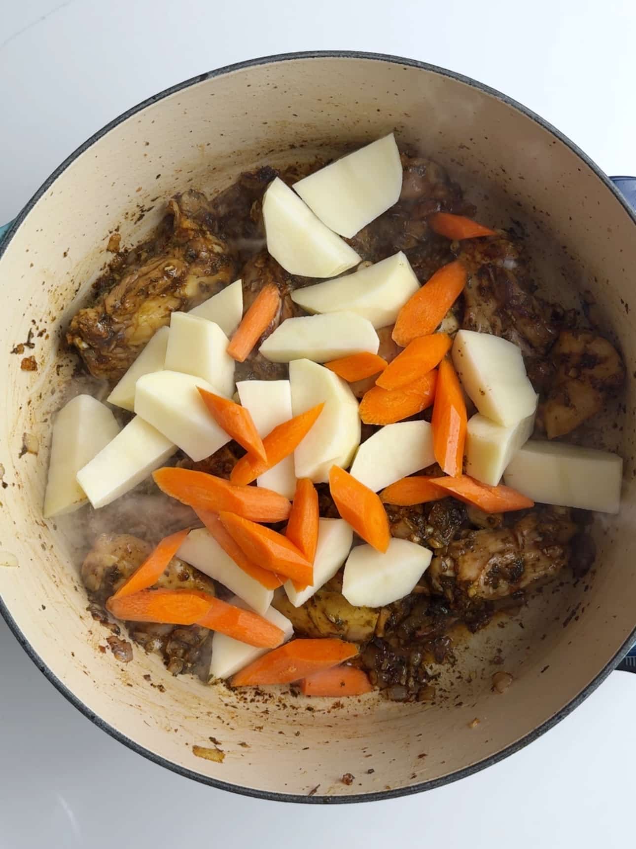 Sliced potatoes and carrots added to seared chicken in a large cast iron pot, for Guyanese Chicken Stew