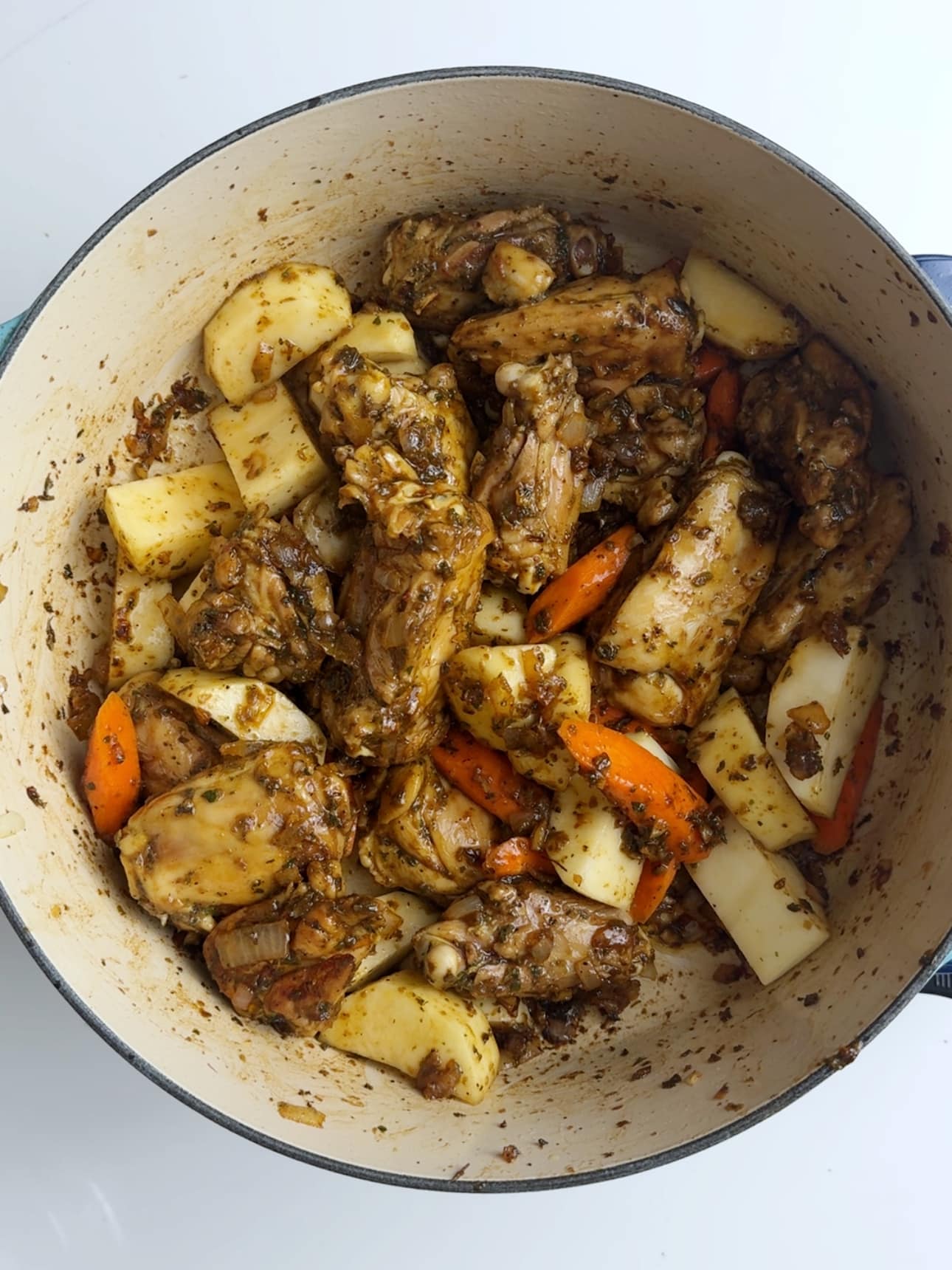 Potatoes and carrots mixed with seared chicken in a cast iron pot for Guyanese chicken stew