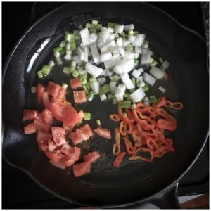 tomatoes, peppers, and onions sautéing in a skillet
