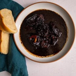 Slow cooker pepperpot in a bowl on a white background with a few slices of plait bread resting on a green napkin