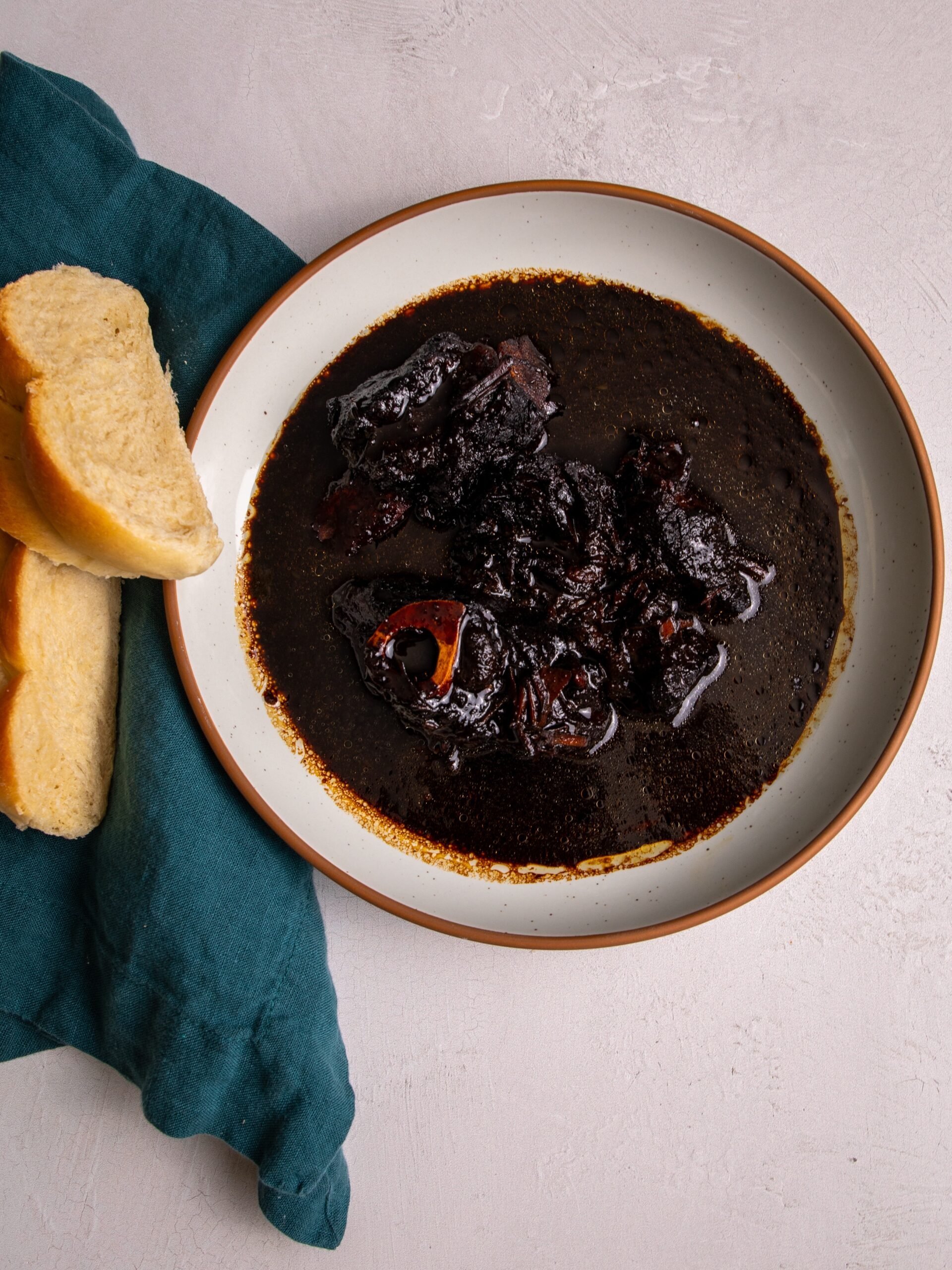 Slow cooker pepperpot in a bowl on a white background with a few slices of plait bread resting on a green napkin