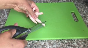 using kitchen shears to prepare chicken foot over a cutting board