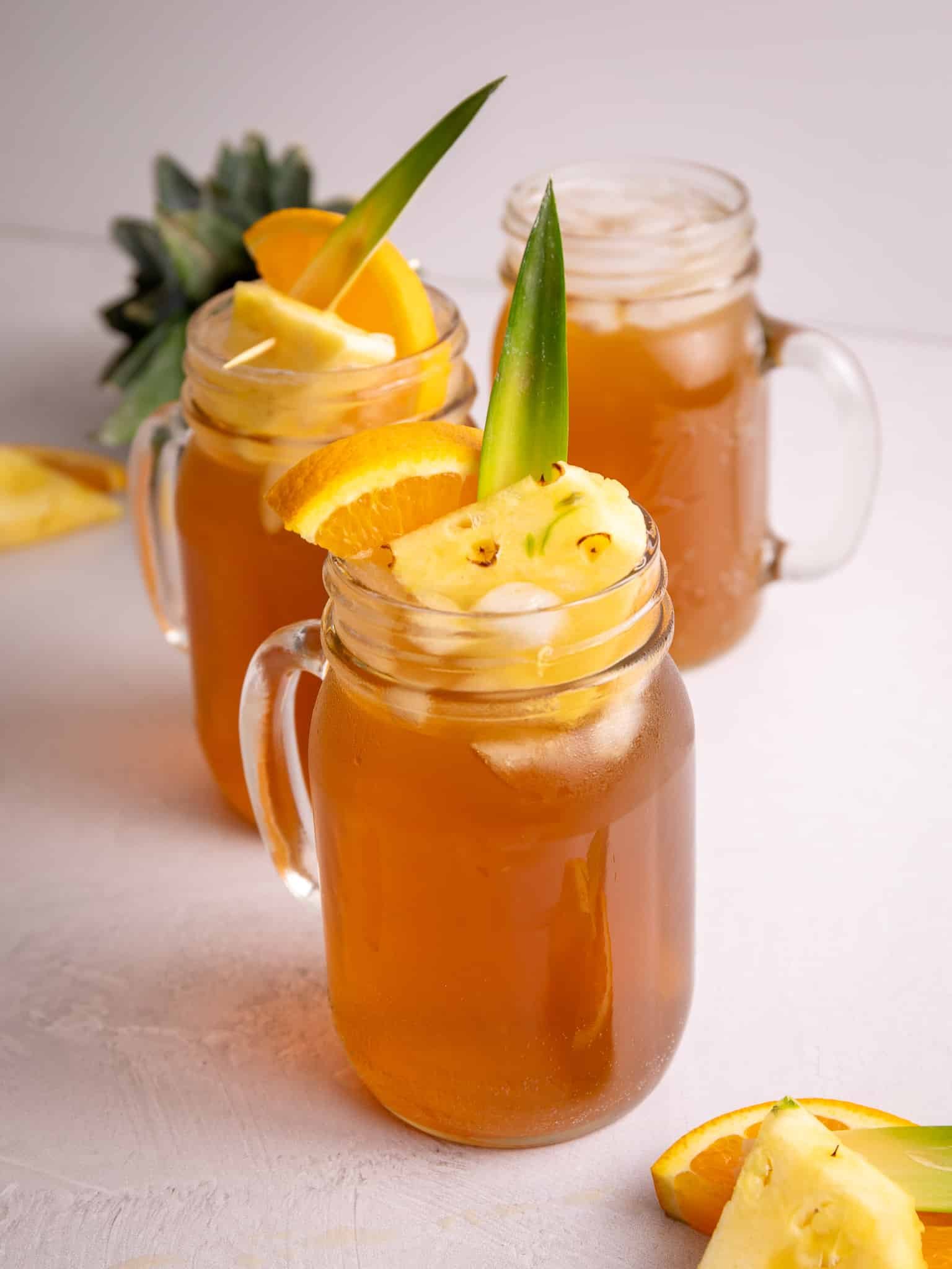 Three glasses of pineapple drink garnished with oranges and pineapples.