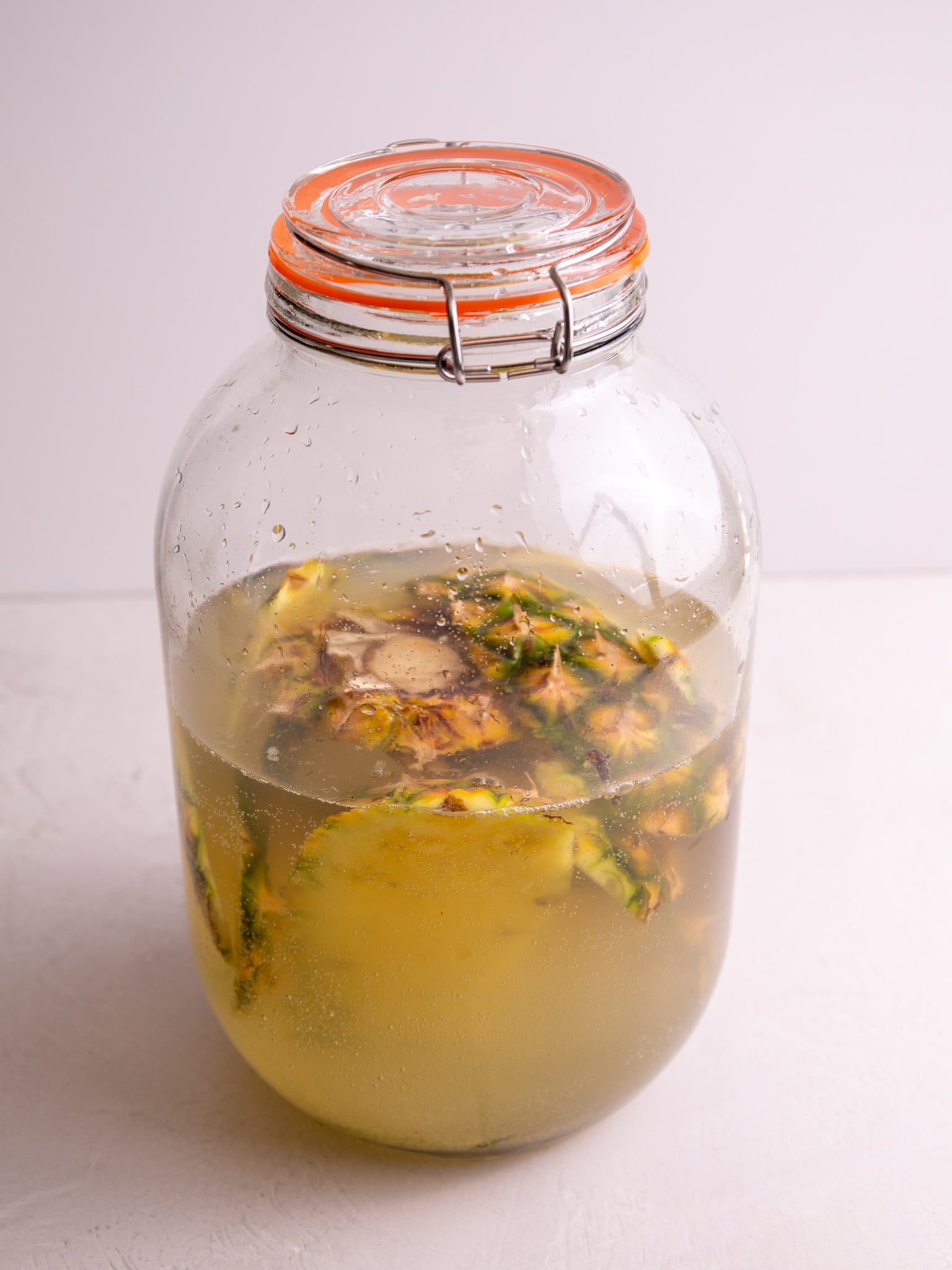 Large glass jar filled with pineapple peels and cores fermenting in lightly fizzy liquid.