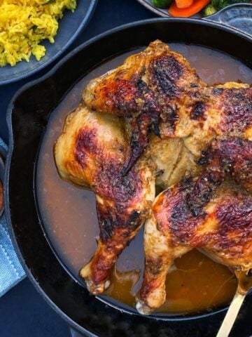 Roasted spatchcocked chicken in a skillet, with peeks of sides