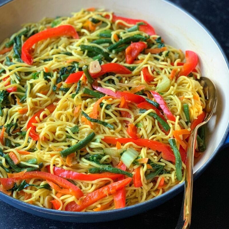 Vegetable chow mein in a large skillet with a golden serving spoon.