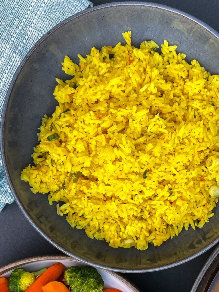 Overhead view of fluffy yellow rice in a black bowl next to other dishes.