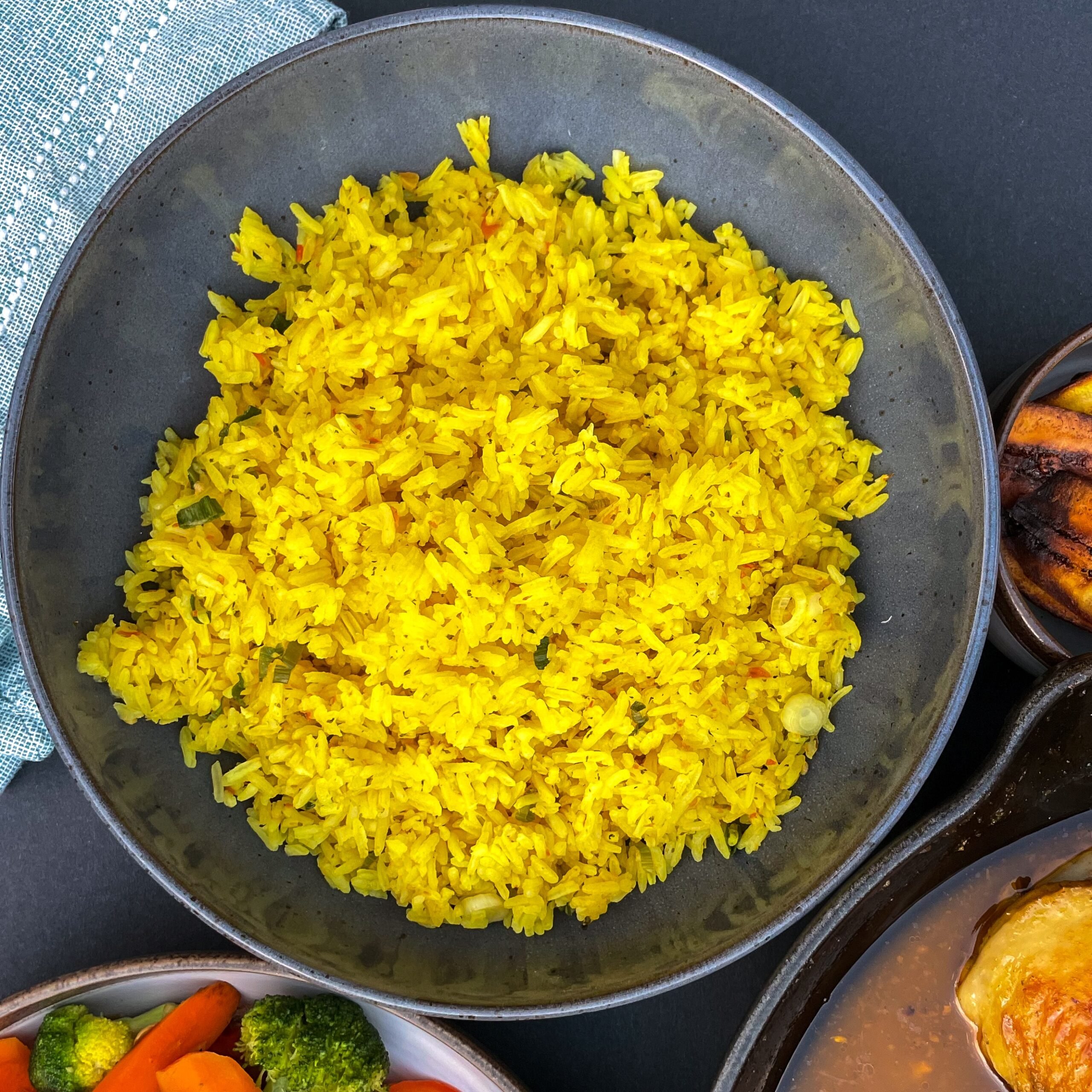 Overhead view of fluffy yellow rice in a black bowl next to other dishes.