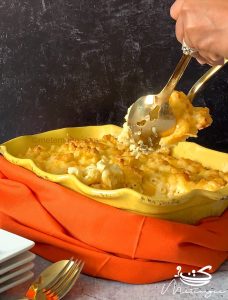 using two large spoons to gather macaroni and cheese from a casserole dish