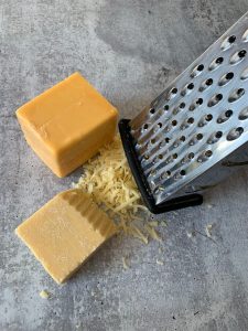 a grater next to two blocks of cheddar