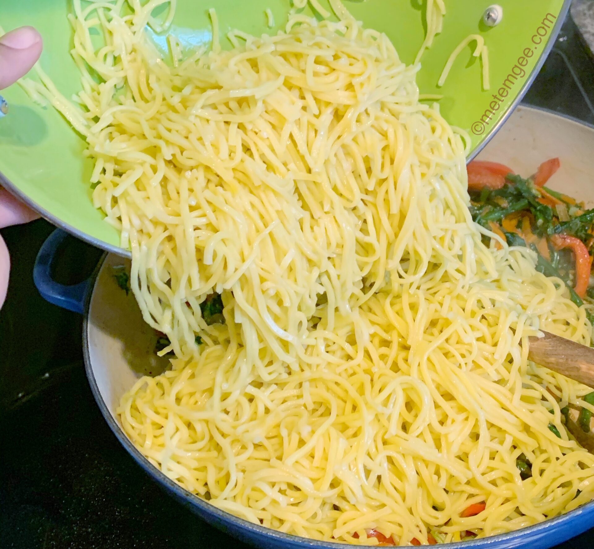 chow mein noodles being added to a pan full of sautéed vegetables 