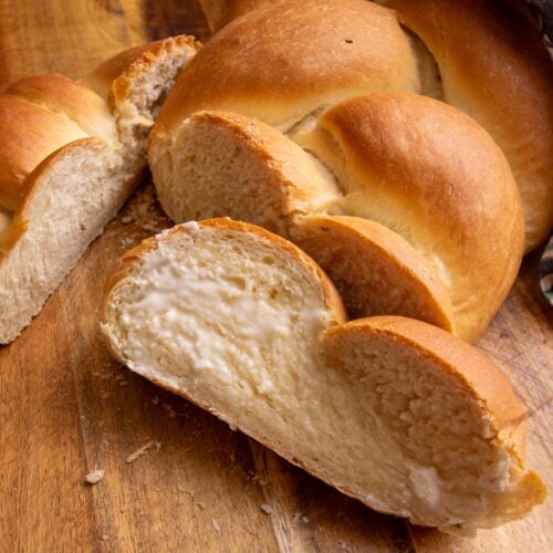 Plait bread sliced up with butter on a brown cutting board and a multi-colored cotton napkin is in the upper right corner.
