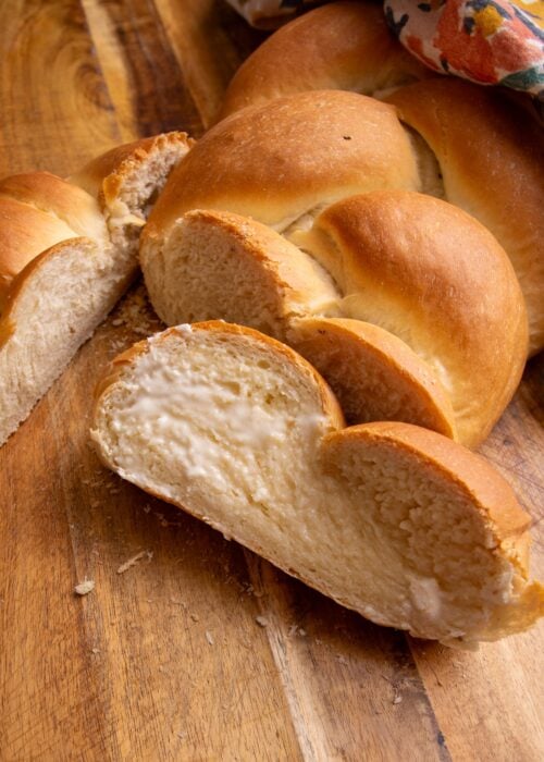 Plait bread sliced up with butter on a brown cutting board and a multi-colored cotton napkin is in the upper right corner.