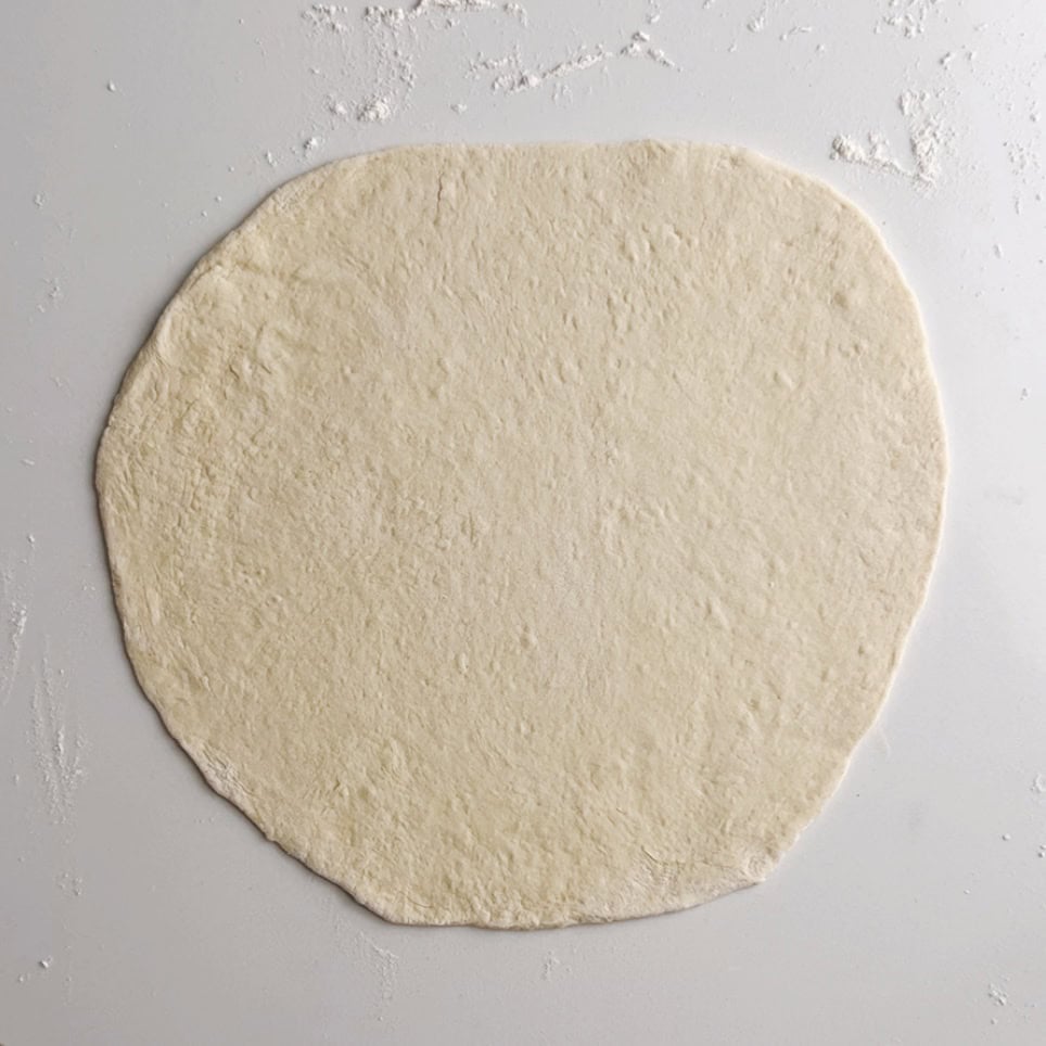 roll a piece of dough out until it is a large, round, flat disk
