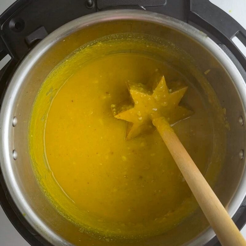 Instant Pot filled with yellow Guyanese dhal with a wooden Dhal Gutney off to the right, sitting in the pot and covered in dhal