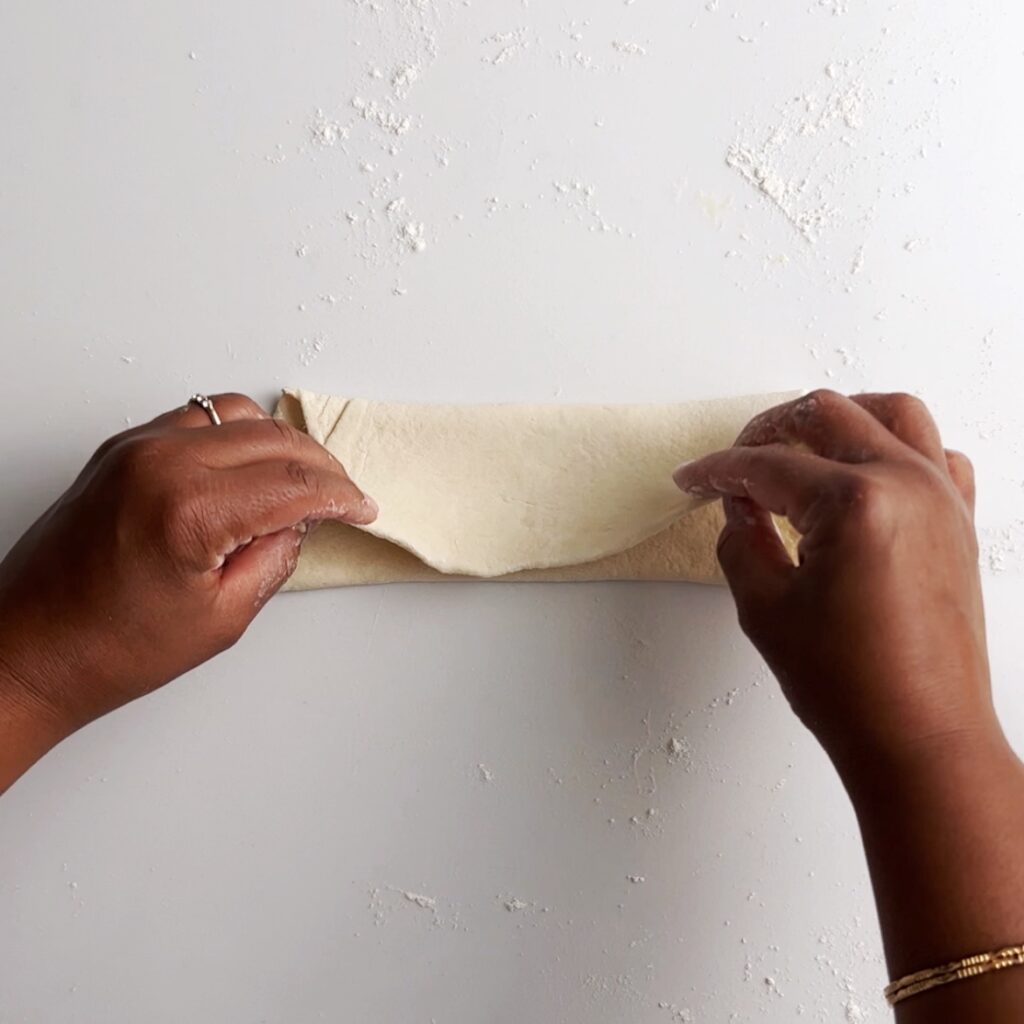 brown hands folding roti dough over into a rectangle