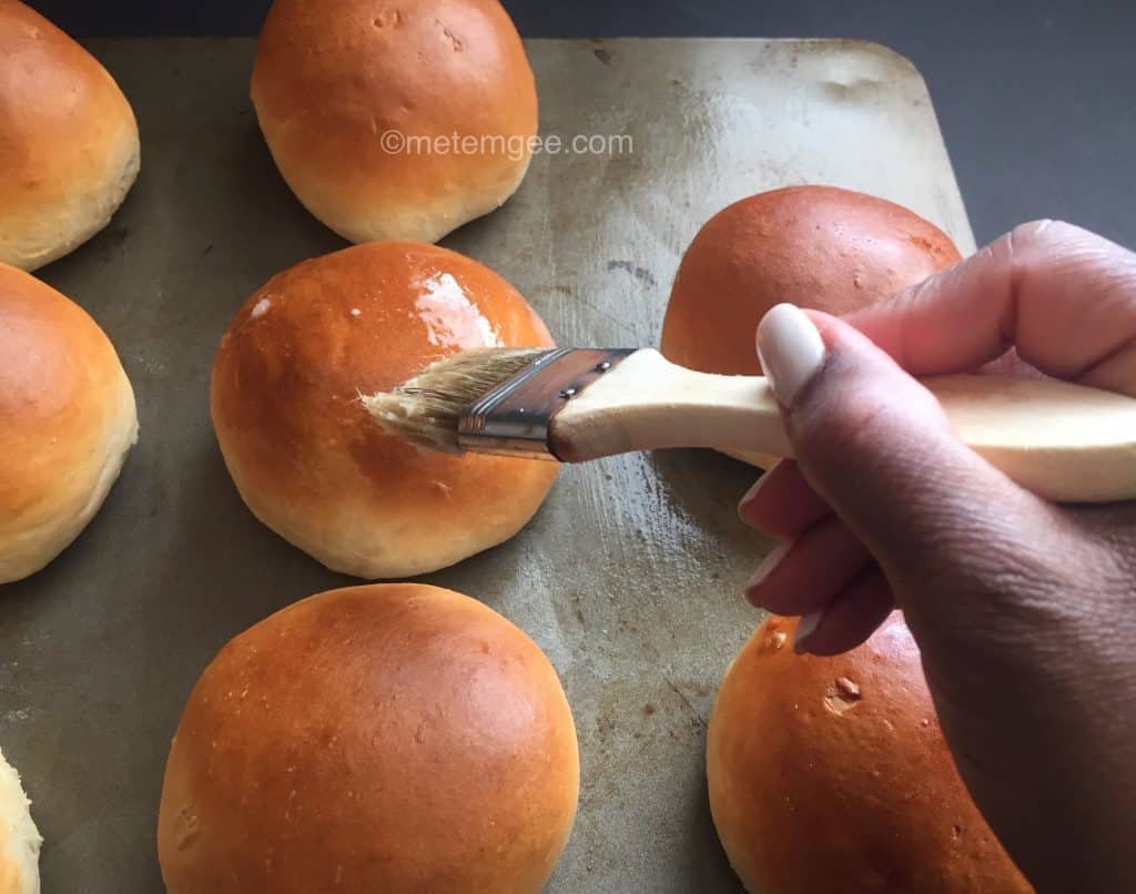 brushing freshly baked tennis rolls with butter