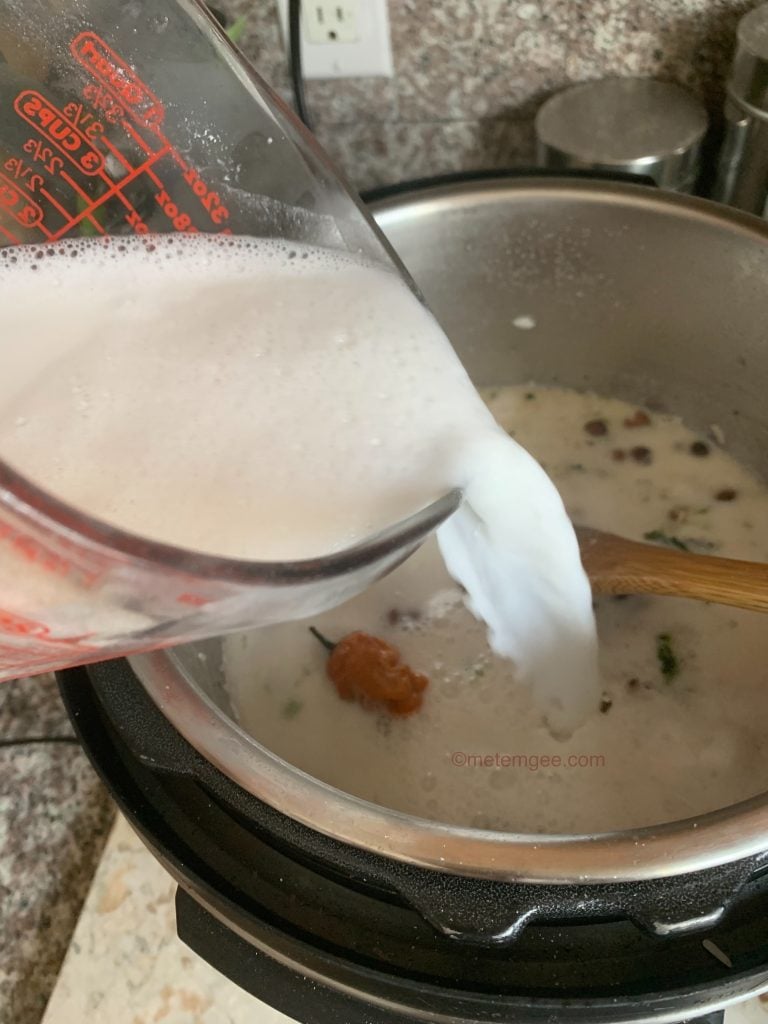 a measuring cup of coconut milk being poured into an instant pot for rice and peas