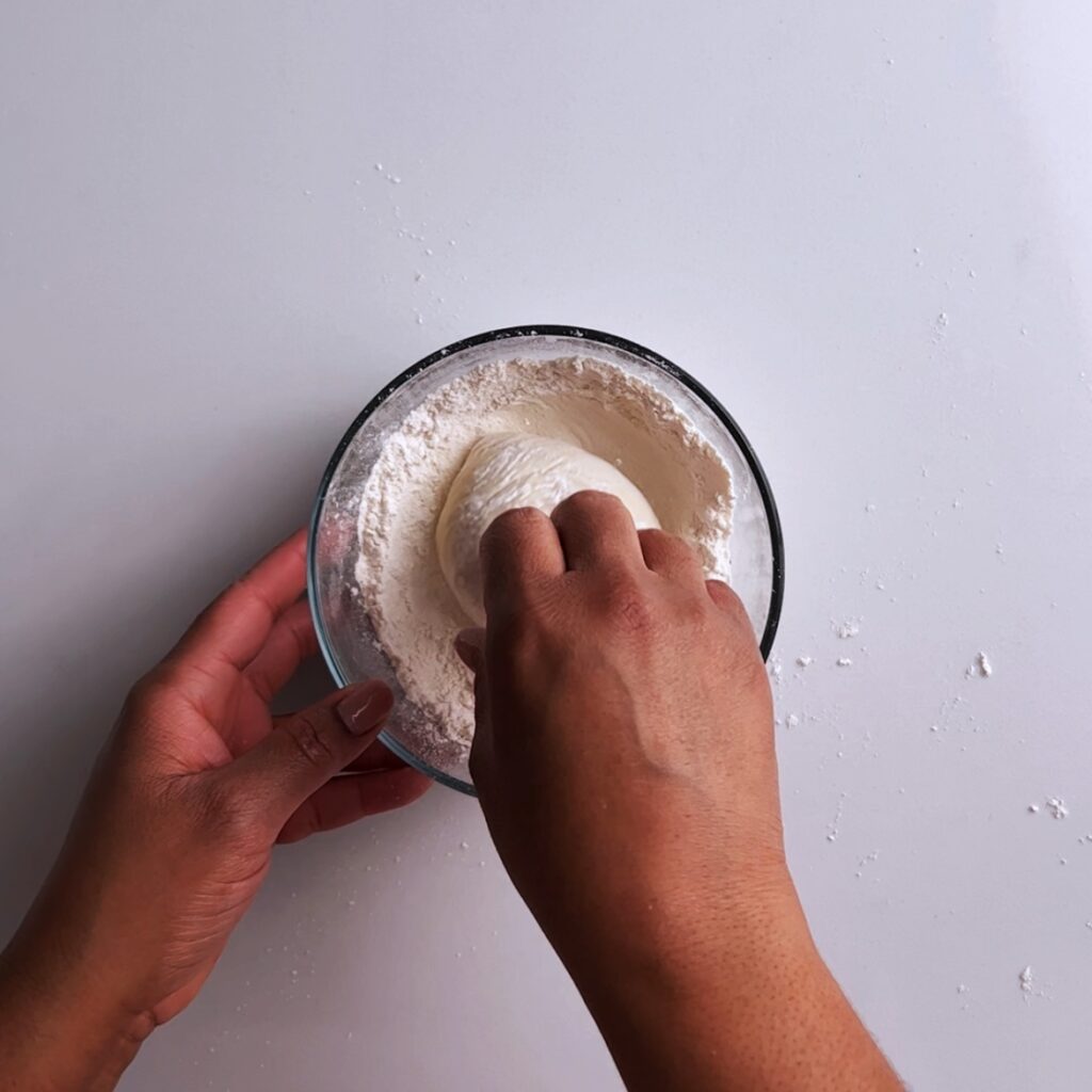 stuffed potato roti rolling into flour in a bowl