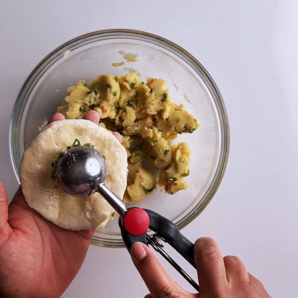 Scooping potato filling into potato roti with a cookie scoop