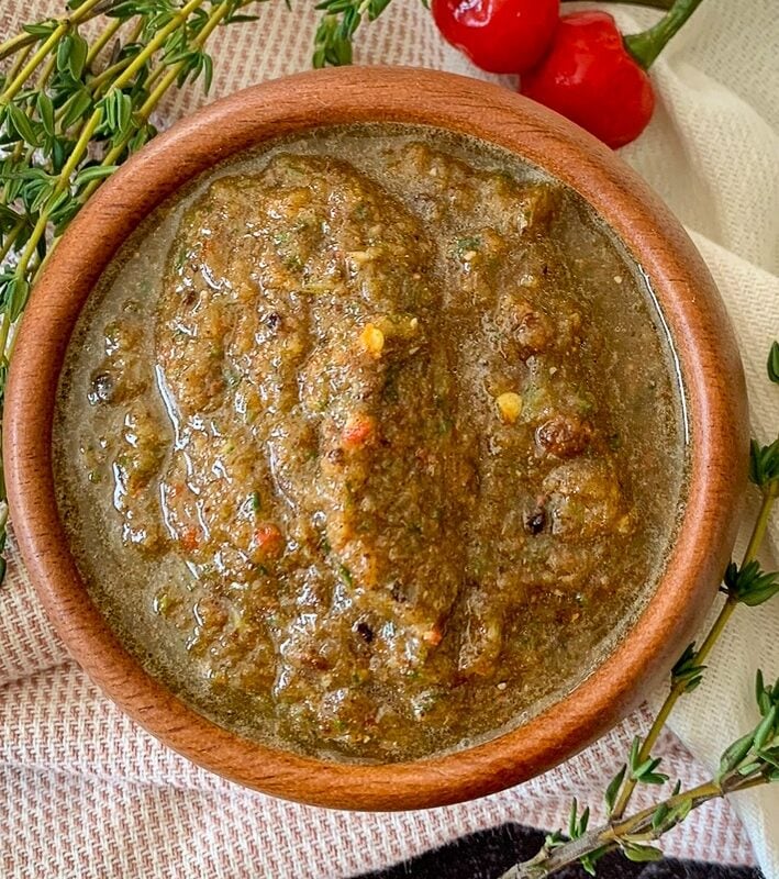 Bowl of homemade Jamaican jerk seasoning paste garnished with thyme and Scotch bonnet peppers.