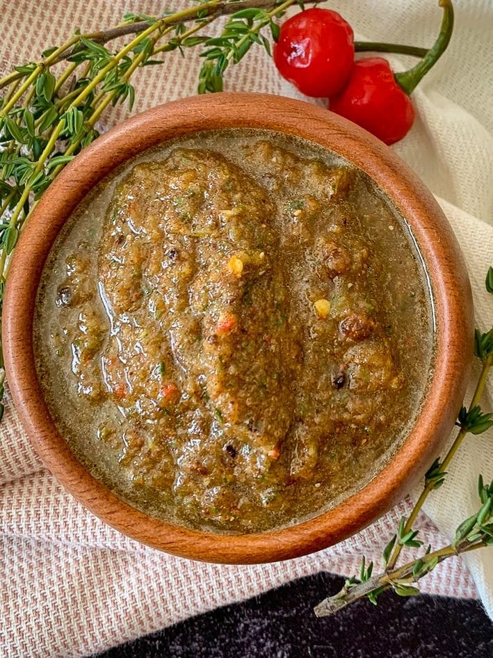 Bowl of homemade Jamaican jerk seasoning paste garnished with thyme and Scotch bonnet peppers.