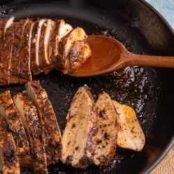 Juicy sliced jerk chicken breast with charred seasoning in a cast iron skillet, resting on a wooden spoon