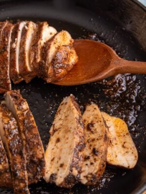 Juicy sliced jerk chicken breast with charred seasoning in a cast iron skillet, resting on a wooden spoon