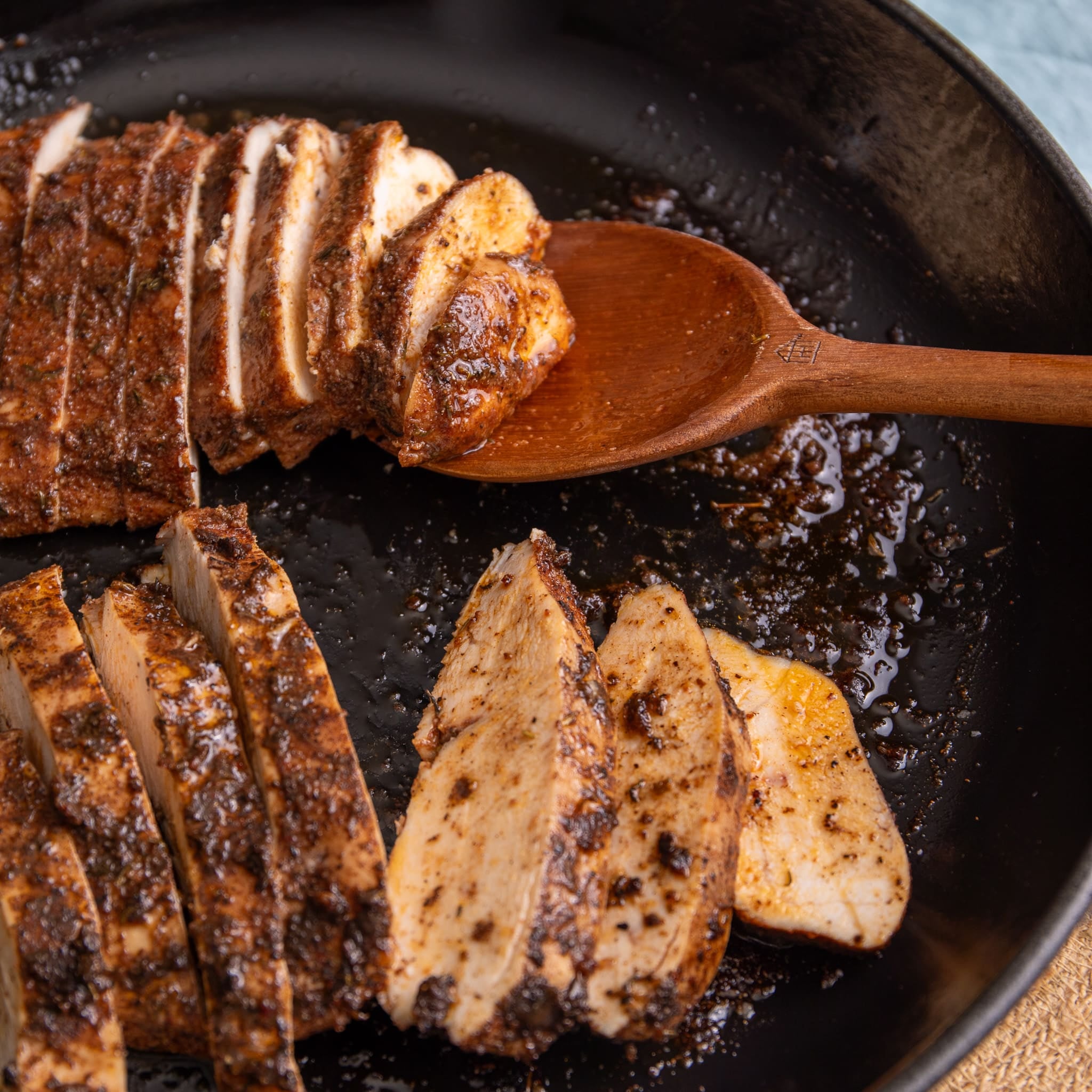 Juicy sliced jerk chicken breast with charred seasoning in a cast iron skillet, resting on a wooden spoon