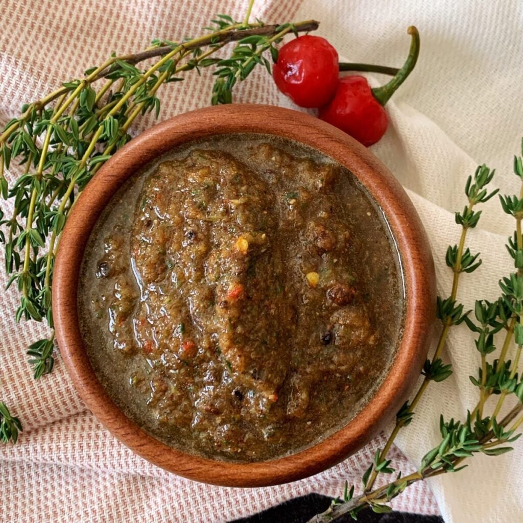 jerk marinade in a wooden bowl on a pink and cream kitchen towel with thyme and wiri wiri pepper