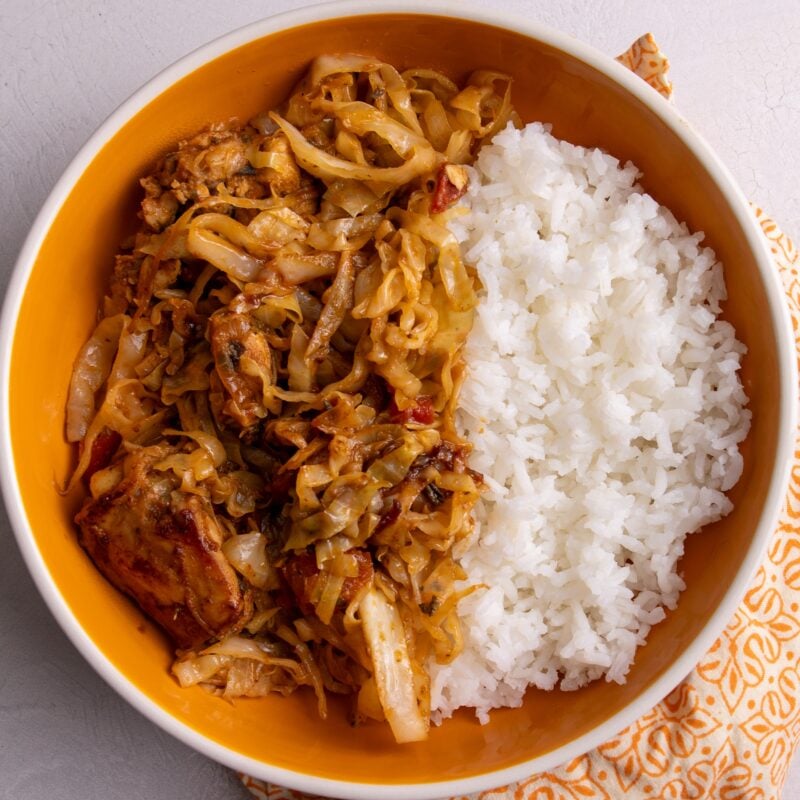 Cabbage and chicken in a yellow bowl with a side of rice. The bowl is on a patterned orange and white napkin against a white background.