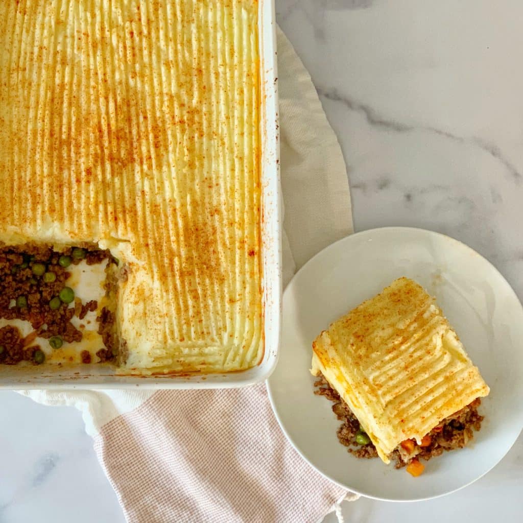 a casserole dish full of shepherd's pie with a slice cut out and placed on a plate beside the dish 