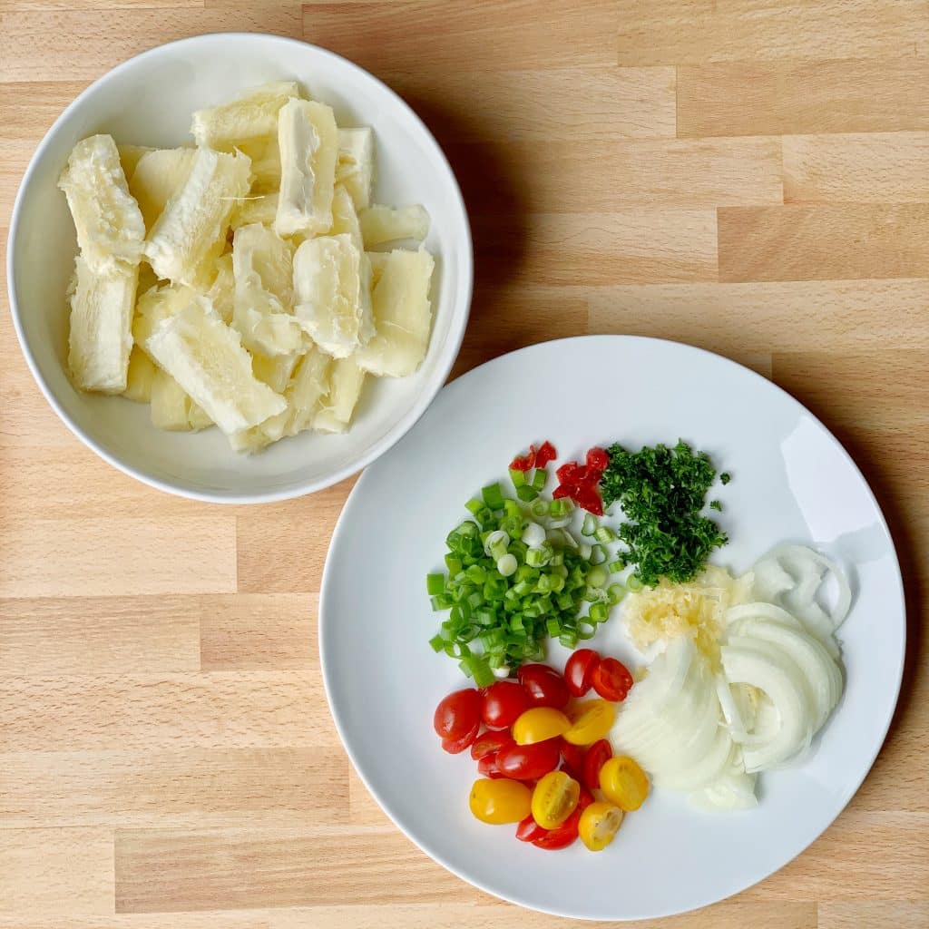 overhead view of peeled and sliced cassava beside a plate of fresh veggies and herbs