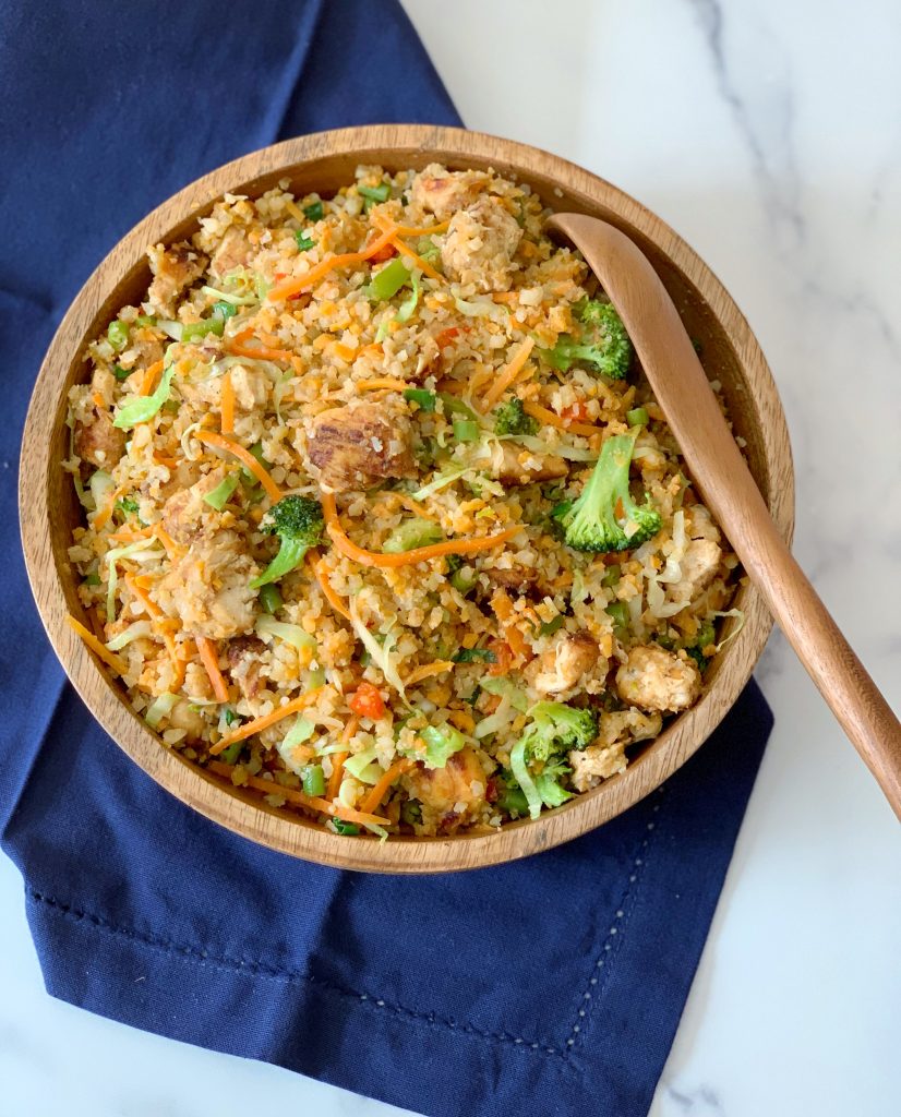 overhead view of a bowl of veggie fried rice with chicken with a wooden spoon inserted