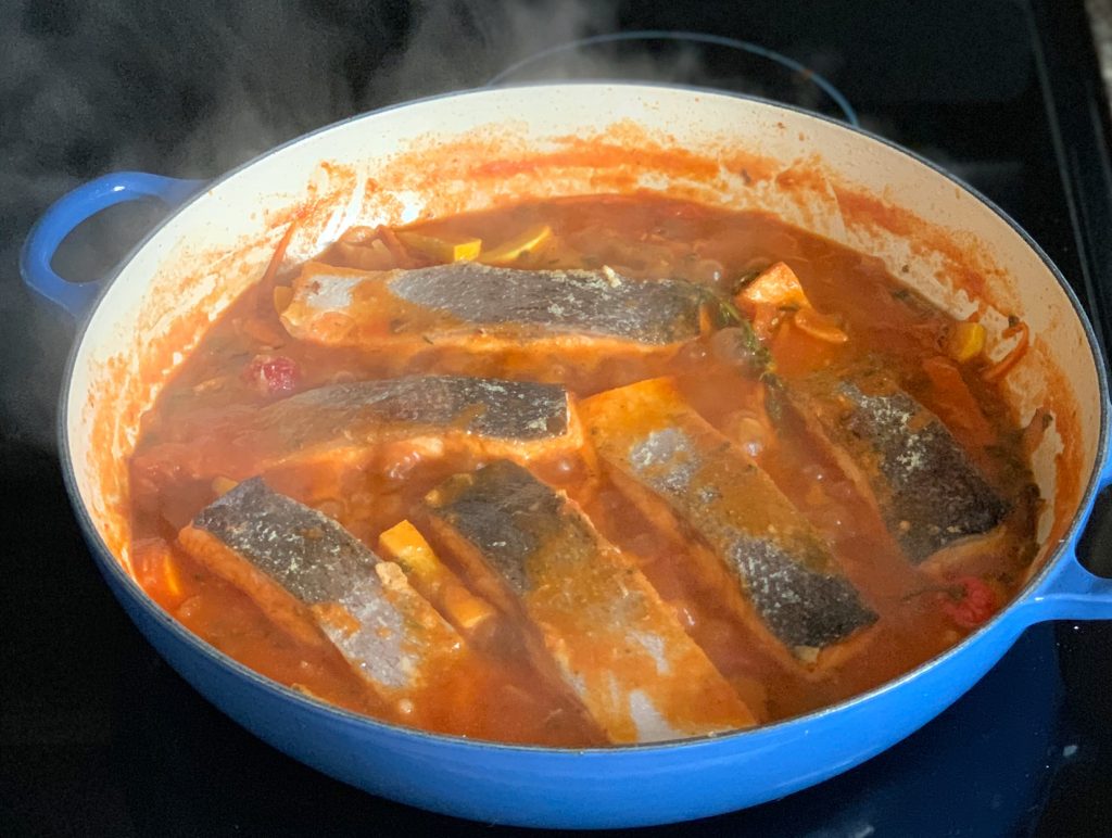 salmon simmering face down in a red stew broth