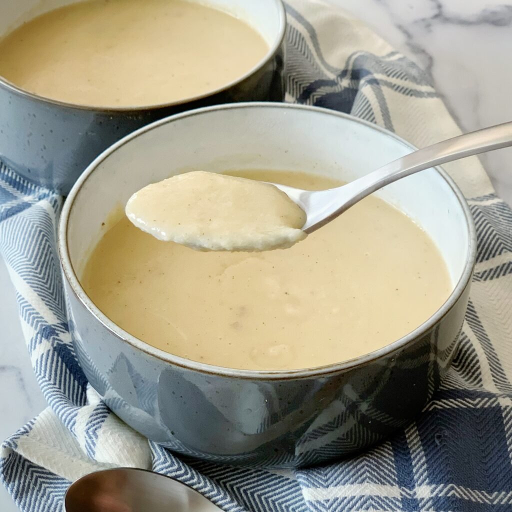 a pot of plantain porridge with a spoonful of porridge hovering over the pot