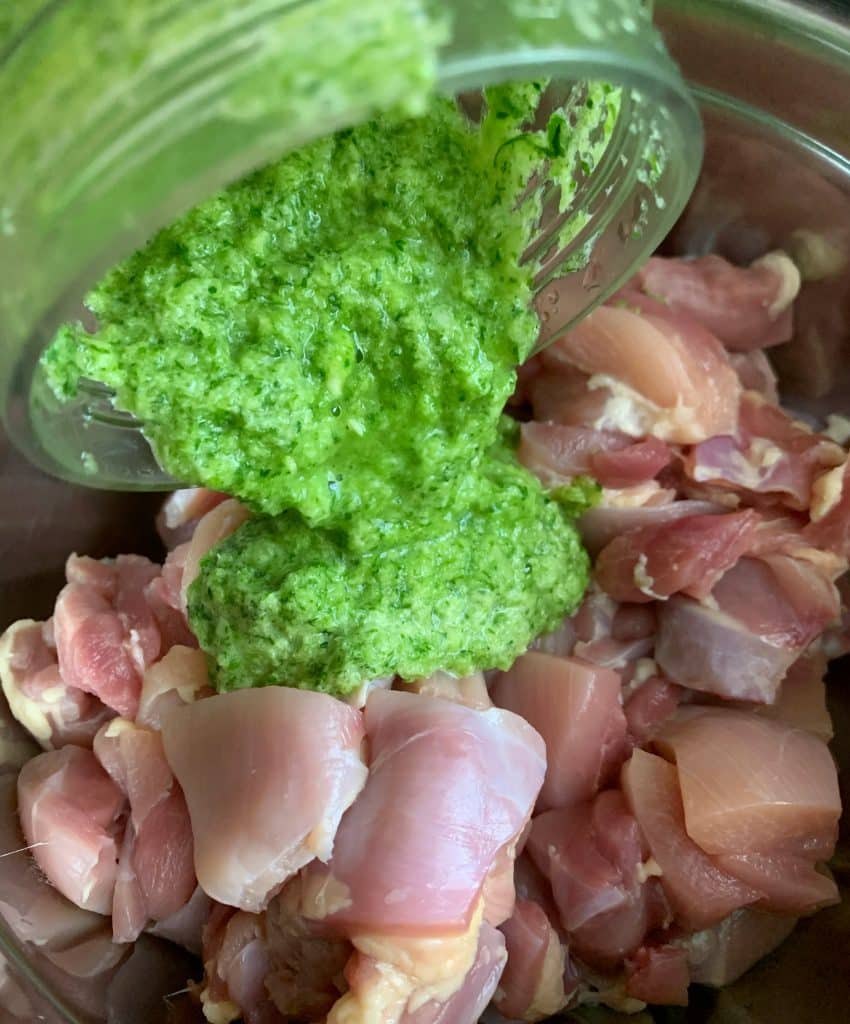 green seasoning being poured over raw chopped chicken thighs